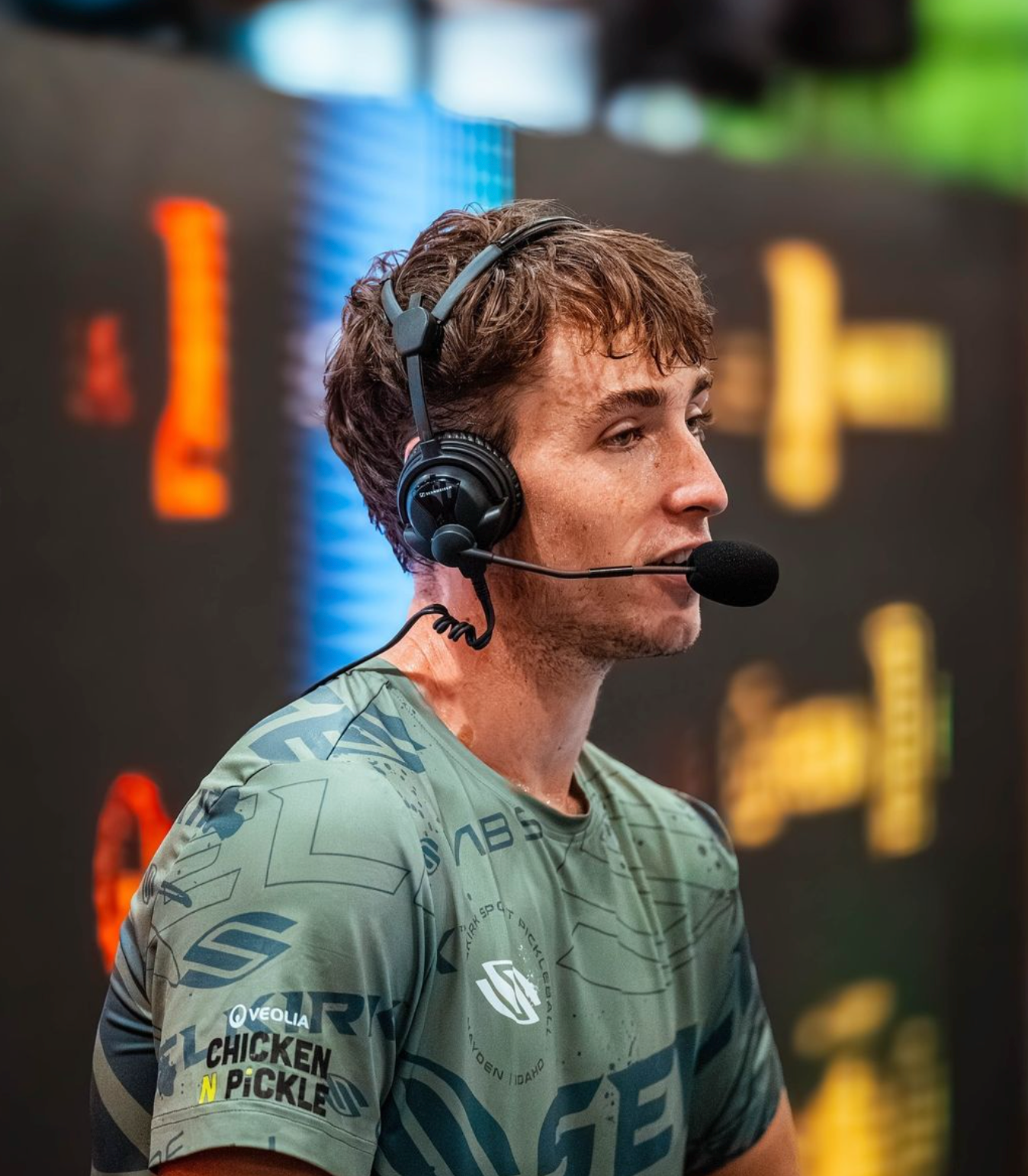 Pickleball player speaking into a headset microphone during a tournament broadcast, wearing a green Selkirk jersey