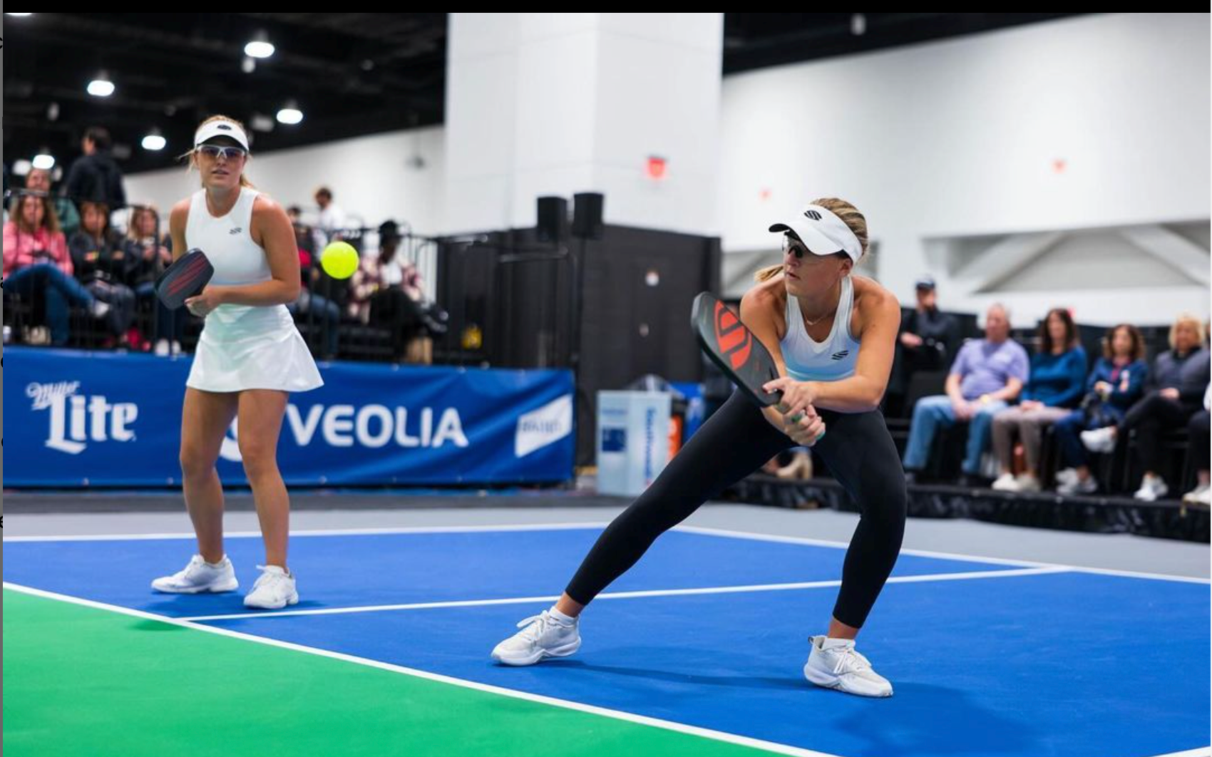Two female pickleball players on court, one preparing to hit a ball.