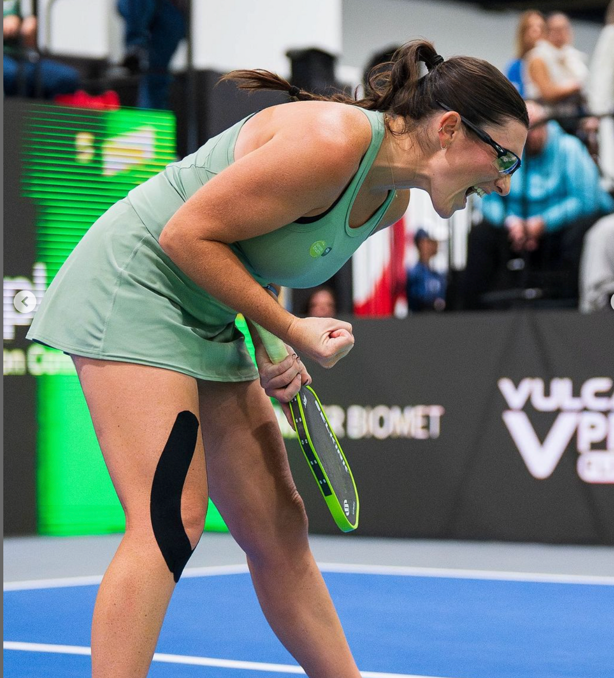 Rachel Rohrabacher bends forward holding a pickleball paddle on a blue court