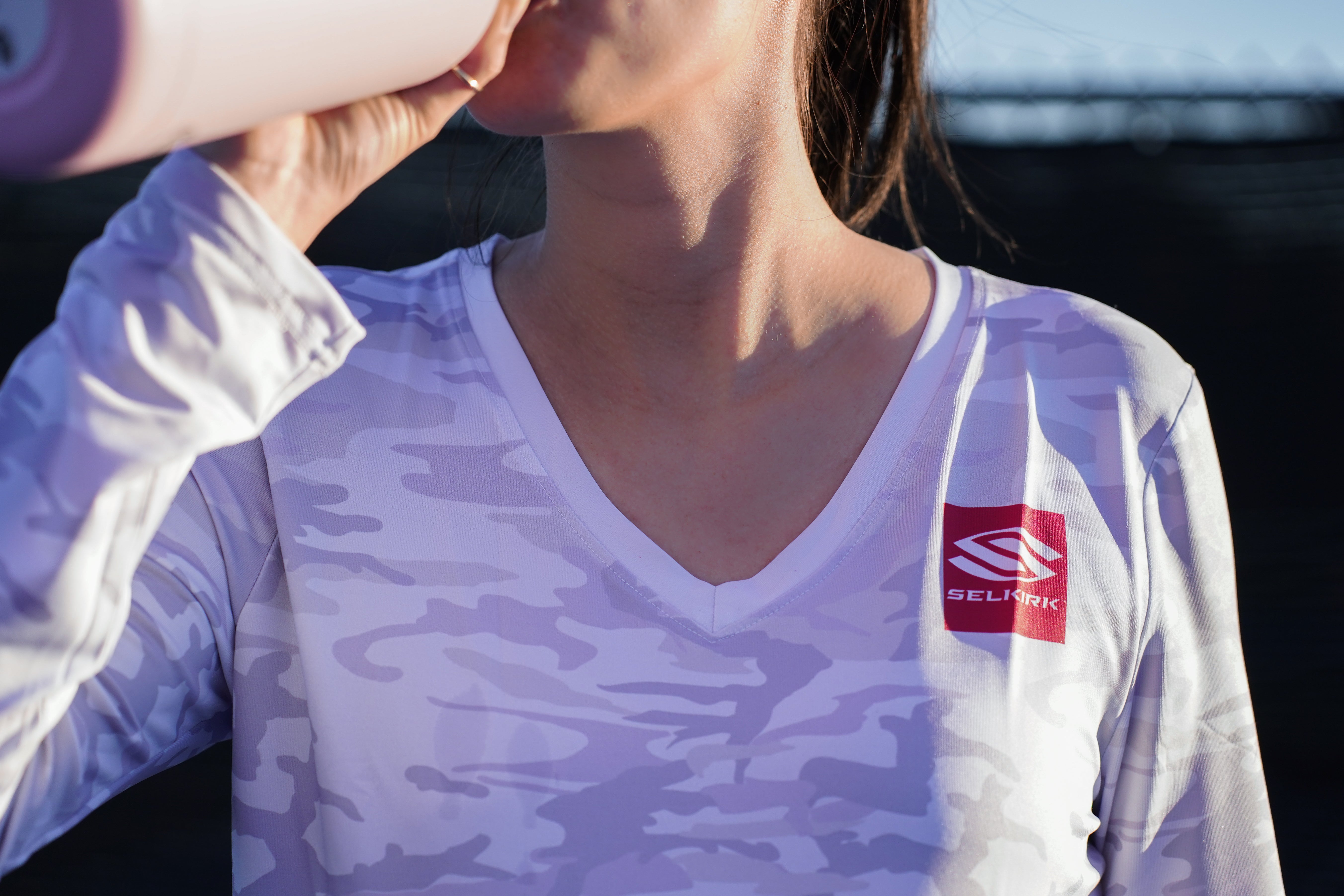 A woman drinking water from a bottle on a pickleball court, emphasizing hydration for performance.