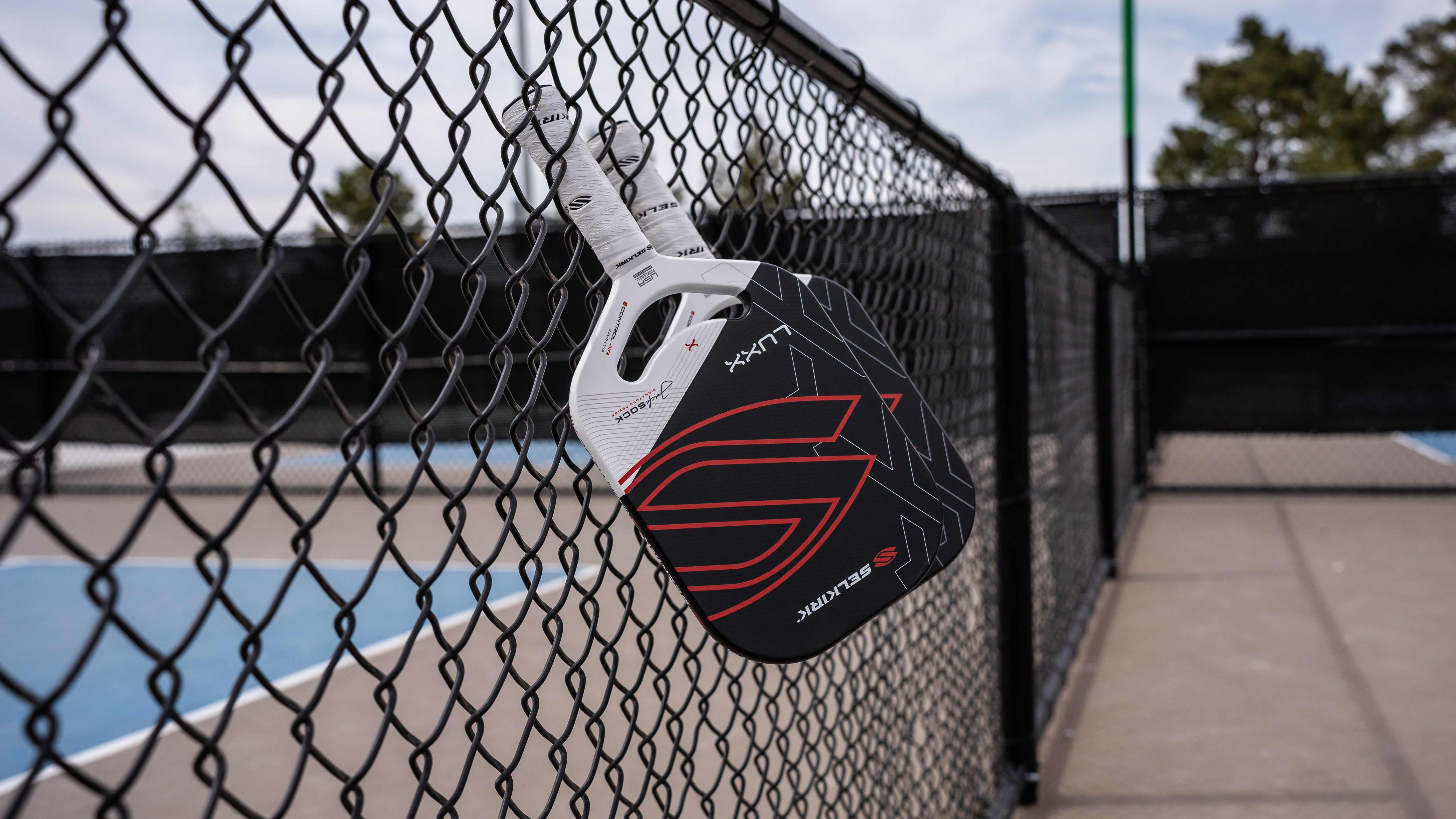 A pickleball paddle hanging on a fence at a court.
