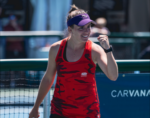 A pickleball player in a red tank top smiles and pumps her fist after scoring.