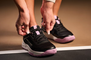 A woman tying her Selkirk pickleball court shoe on an indoor court.
