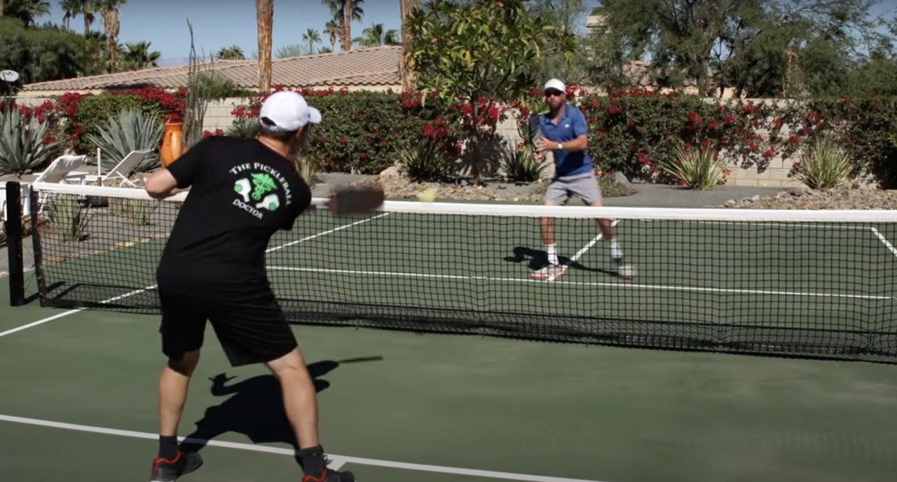 Two players practicing pickleball on a court, one preparing to hit the ball.