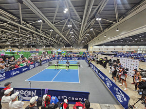 Four pickleball players playing doubles on an indoor NPL court surrounded by spectators, officials, and sponsor banners