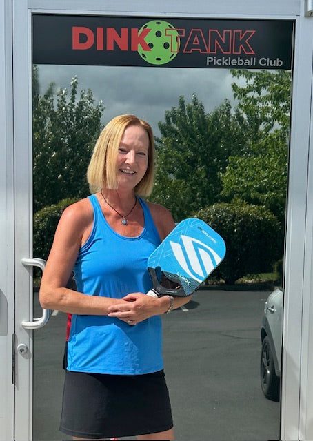 Nancy Mansfield holding a blue pickleball paddle outside Dink Tank Pickleball Club
