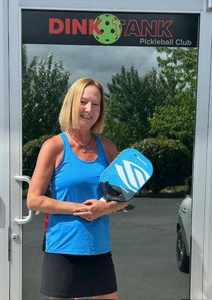 Nancy Mansfield holding a blue pickleball paddle outside Dink Tank Pickleball Club