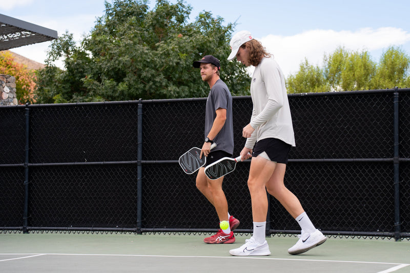 Two pickleball players walk across an outdoor court carrying paddles