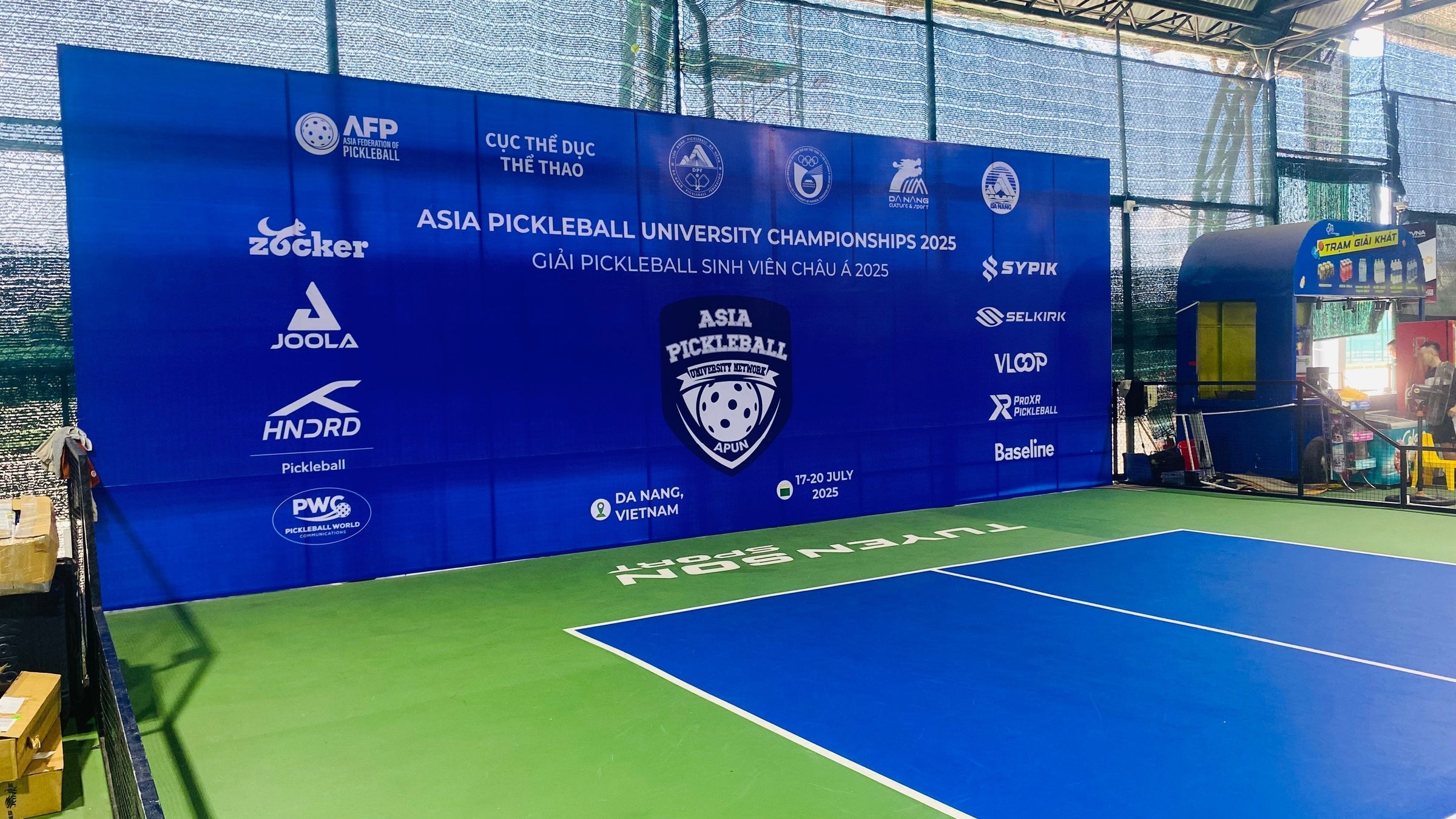 Indoor pickleball court with a large blue sponsor backdrop reading Asia Pickleball University Championships 2025 and a visible Selkirk logo