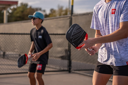Two players practicing pickleball on an outdoor court, foreground player holding a Selkirk paddle