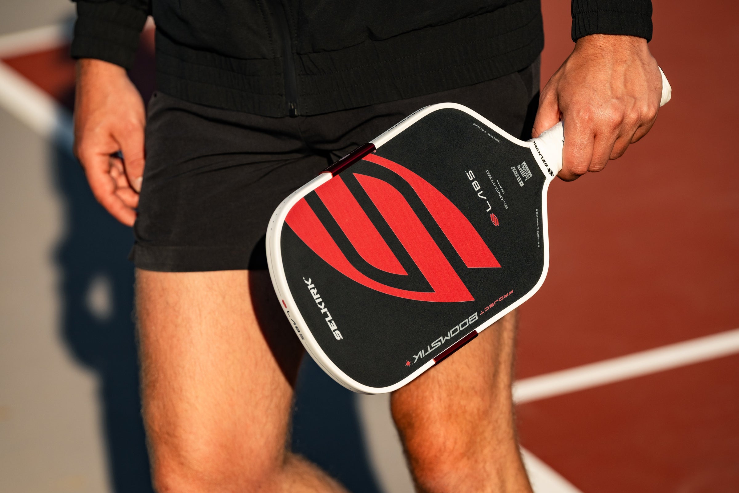 Close view of Selkirk LABS Project Boomstik pickleball paddle with red and black face, held on a pickleball court