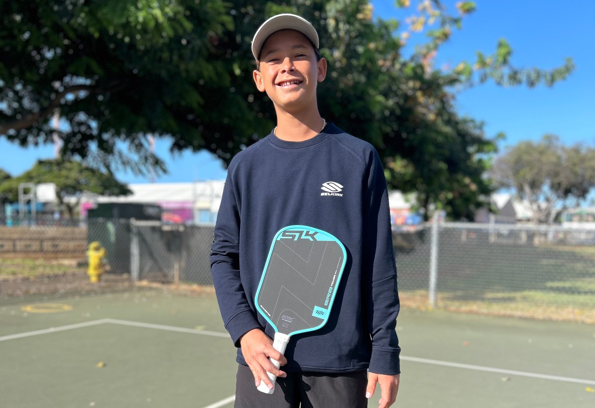 Teen holding a Selkirk SLK pickleball paddle and smiling on an outdoor court
