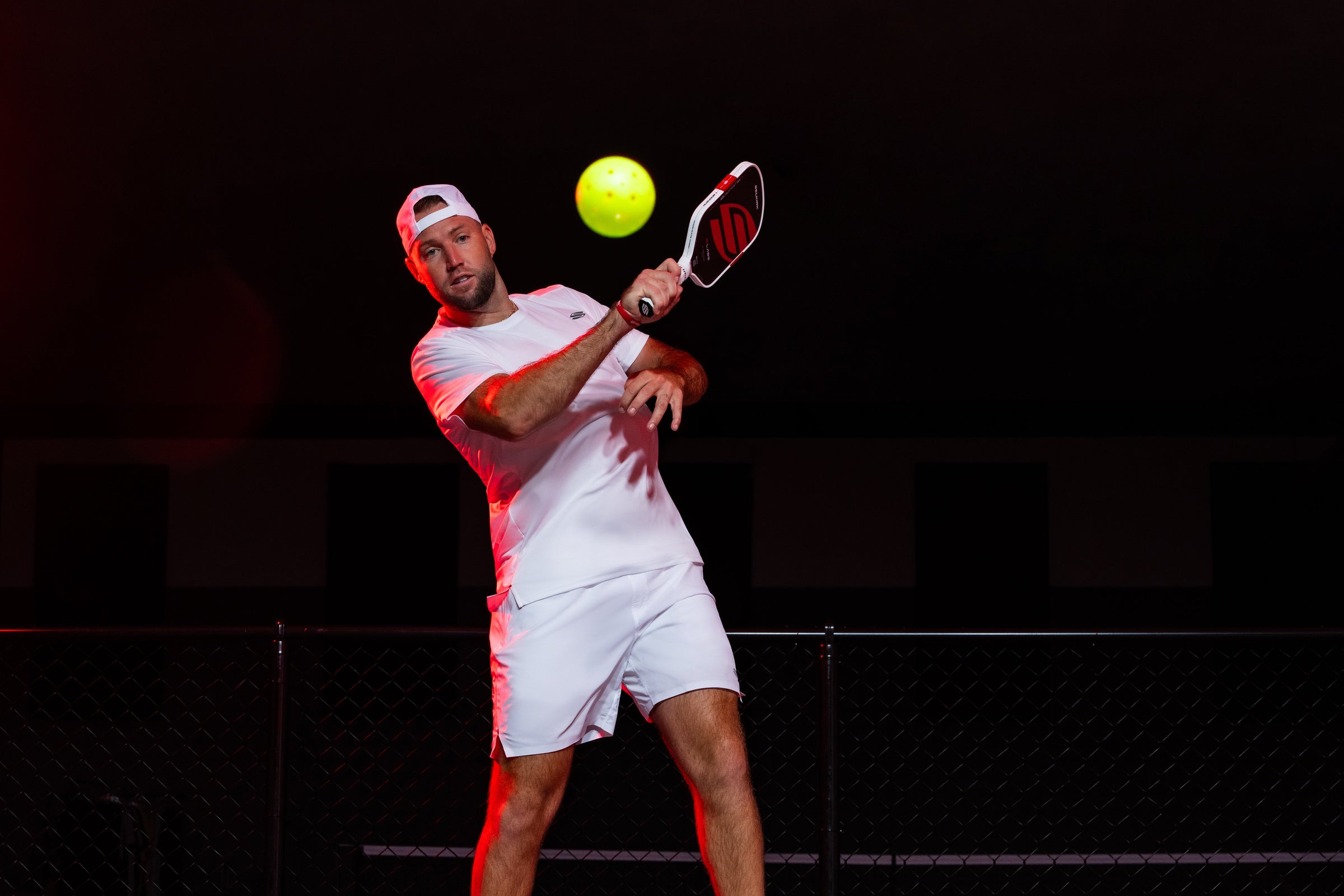 Male pickleball player mid-swing hitting a ball with a Selkirk paddle on a dark indoor court