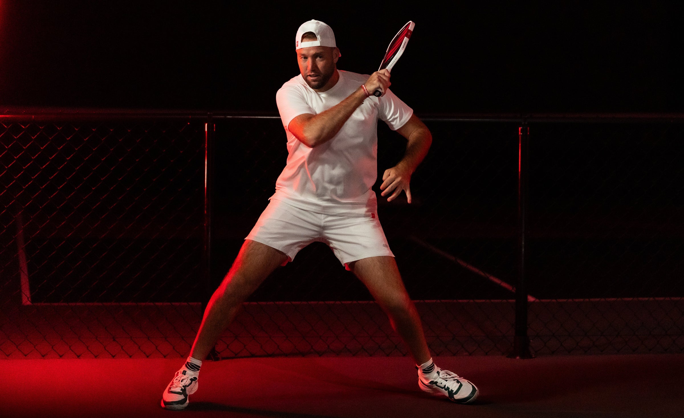 Pickleball player hitting a forehand with a Boomstik paddle on a dark court illuminated by red side lighting