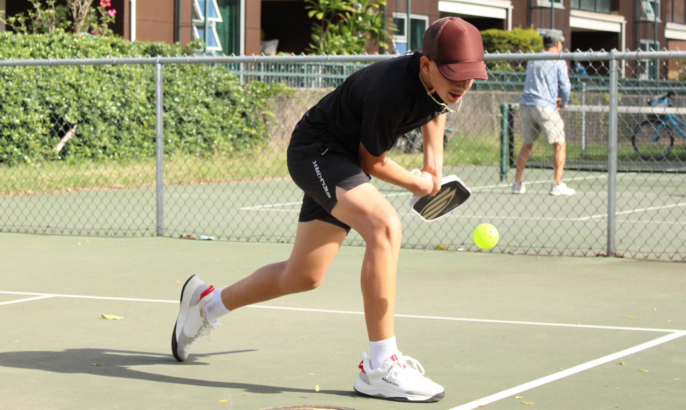 Tama Shimabukuro lunges to hit a pickleball with a paddle on an outdoor court