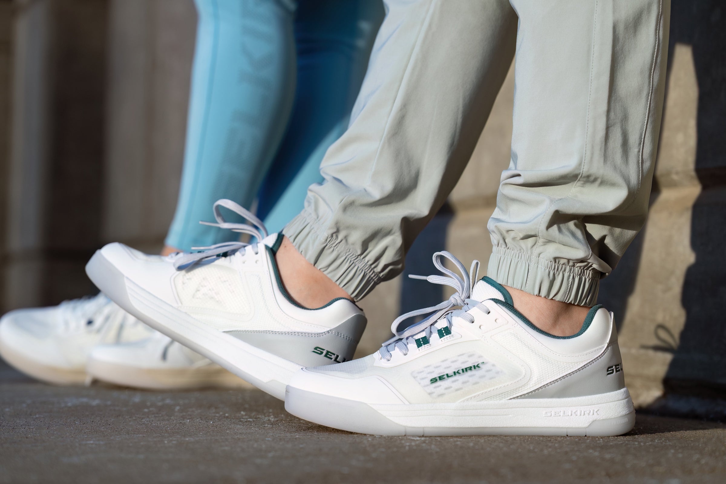 Close-up of white Legacy shoes showcasing teal accents and textured panels with two people wearing them outdoors