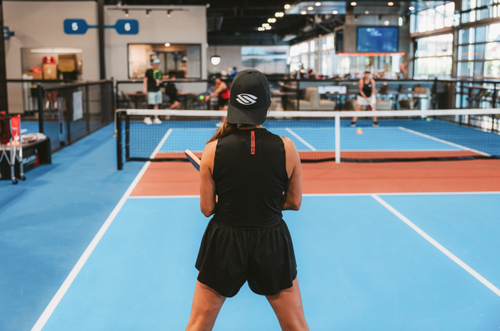 Player preparing to return a pickleball shot on an indoor court, viewed from behind