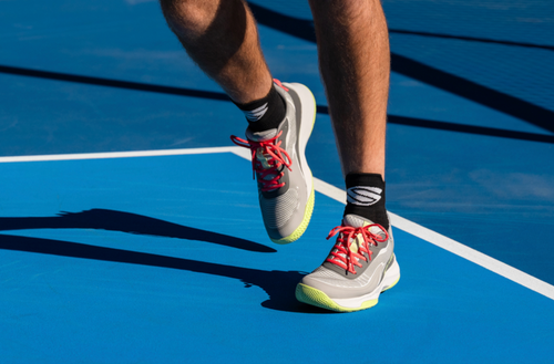 Action view of CourtStrike 3.0 pickleball shoes on feet showing gray upper, neon yellow sole, and red laces on a blue court