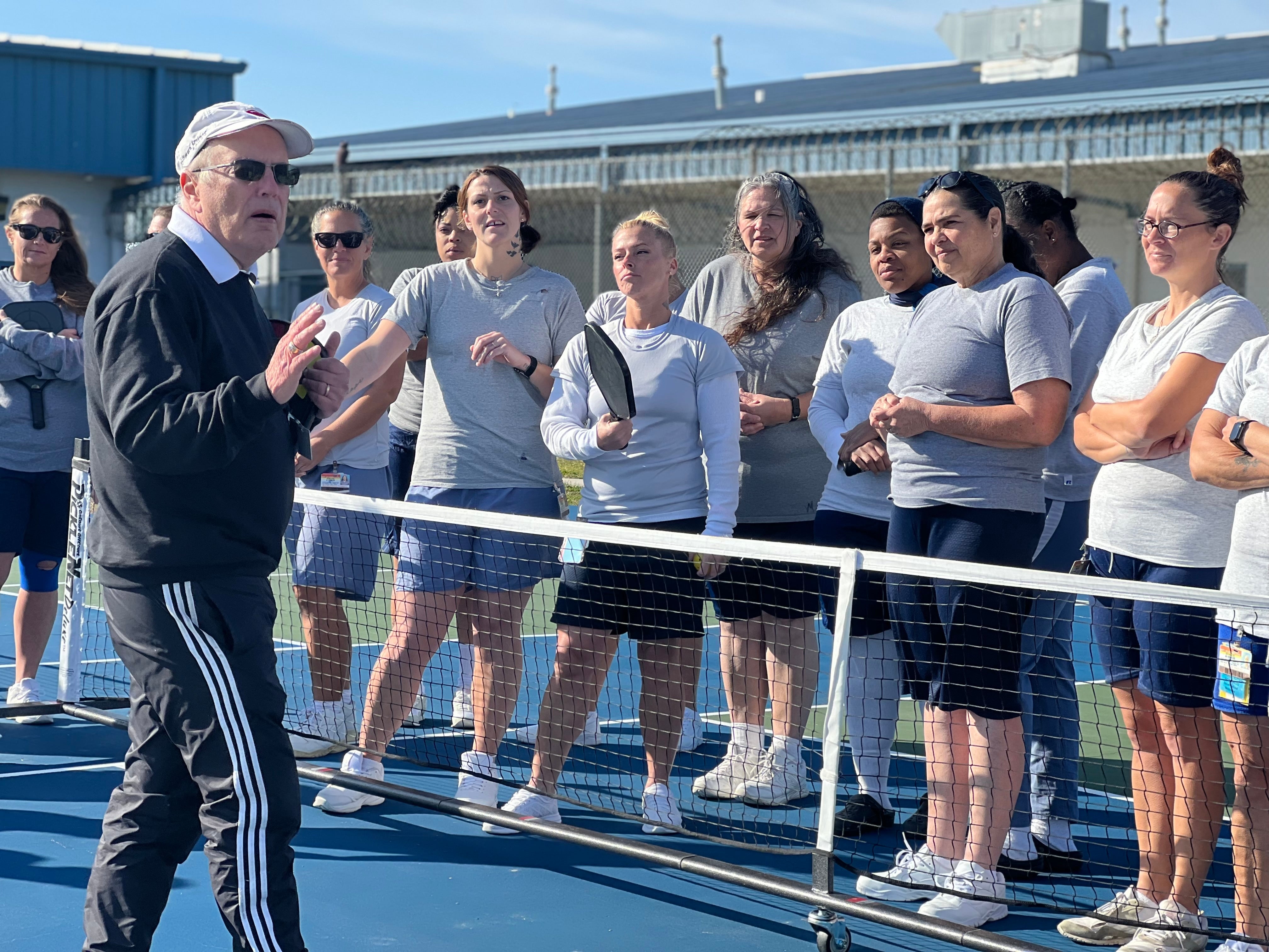 Roger BelAir instructing a group of female inmates in pickleball at a prison facility.