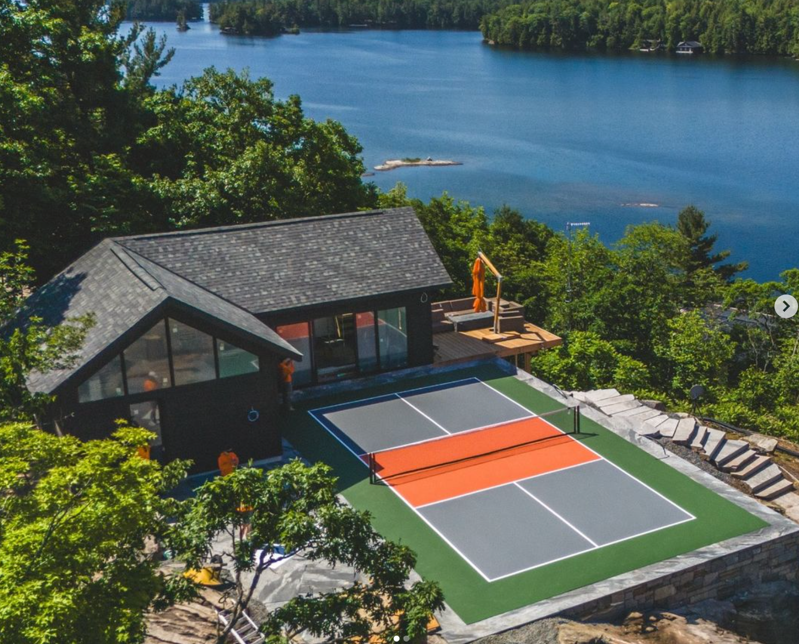 A private pickleball court is positioned near a house overlooking a lake. 