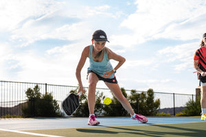 A woman lunges to hit a dink on an outdoor pickleball court. 