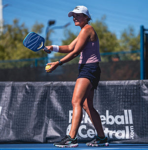 A player preparing to serve in pickleball, holding a paddle and ball on a court.
