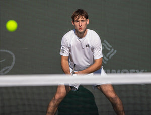 Professional pickleball player Dylan Frazier stands at the baseline of the court ready to receive a ball that is traveling over the net. 