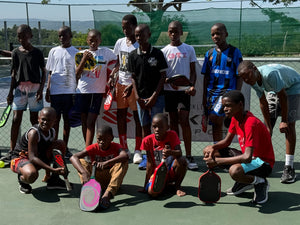 A group of African children holds pickleball paddles and smiles in front of a Selkirk banner. 