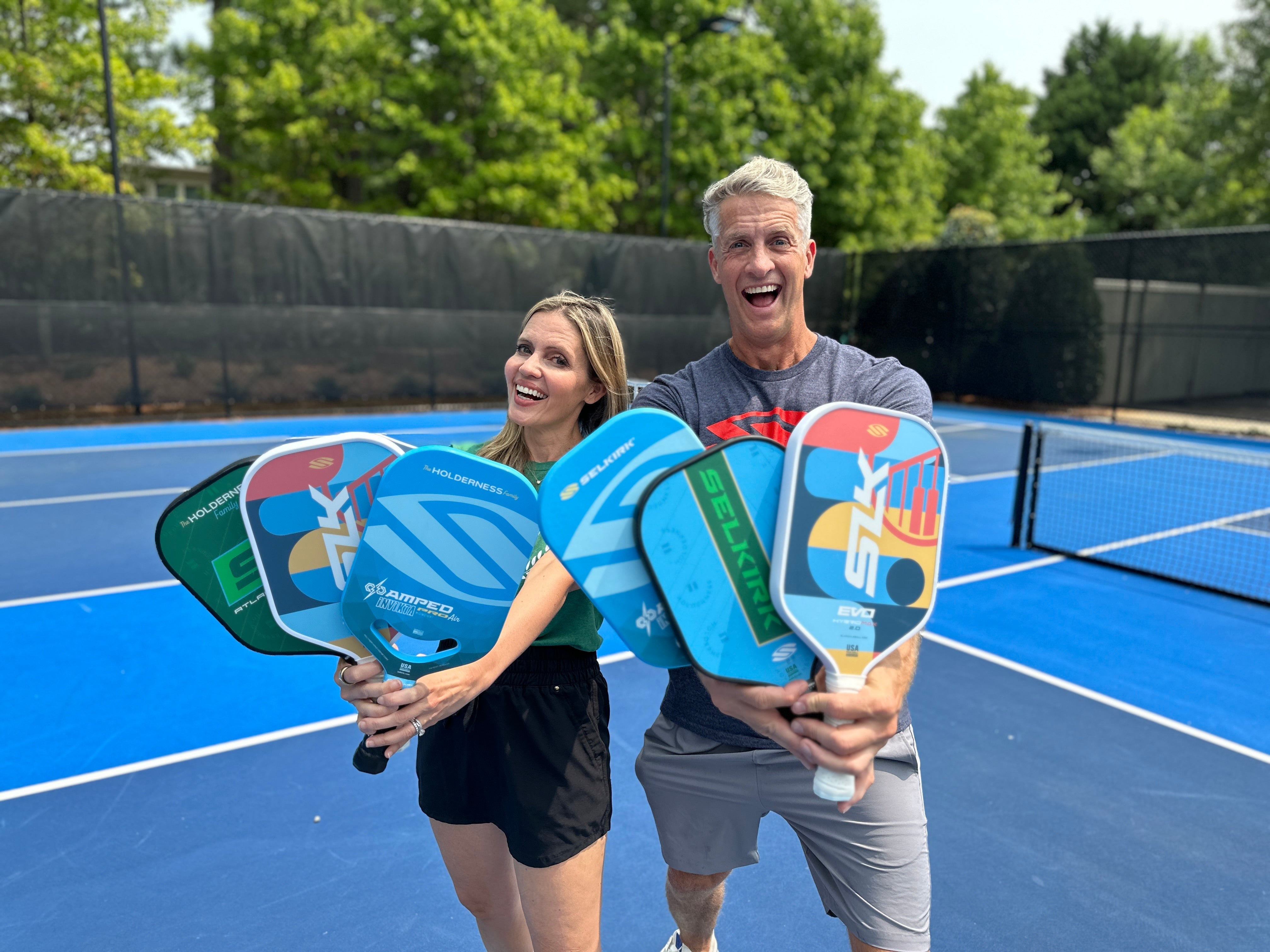 Two people on a pickleball court holding colorful paddles, smiling.