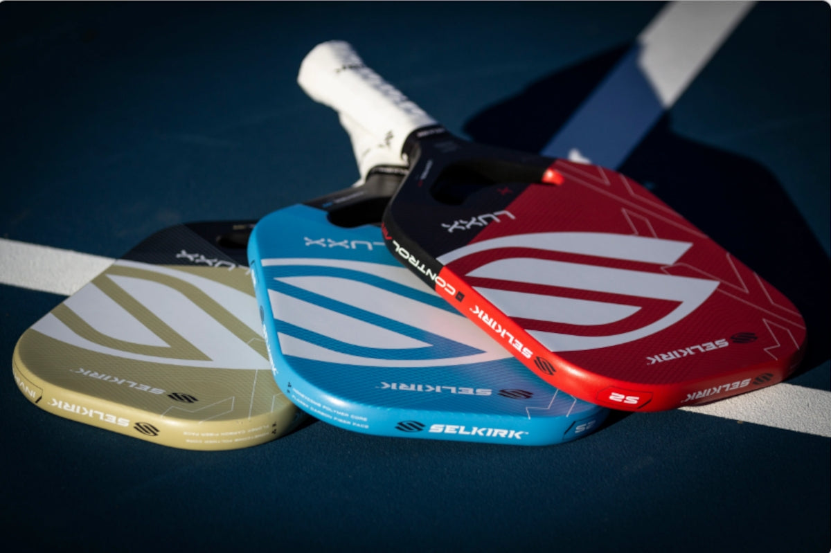 Three Selkirk pickleball paddles: LUXX Control Air in red, blue, and yellow on a court.