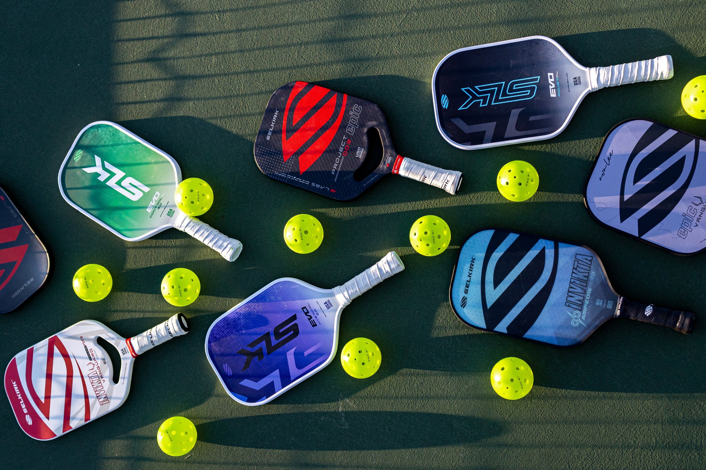 A collection of pickleball paddles and balls on a court surface.
