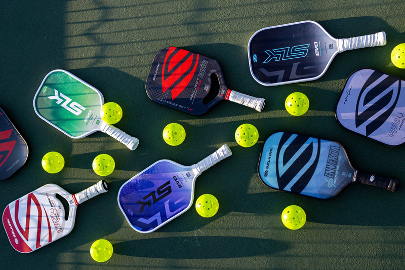 A collection of pickleball paddles and balls on a court surface.