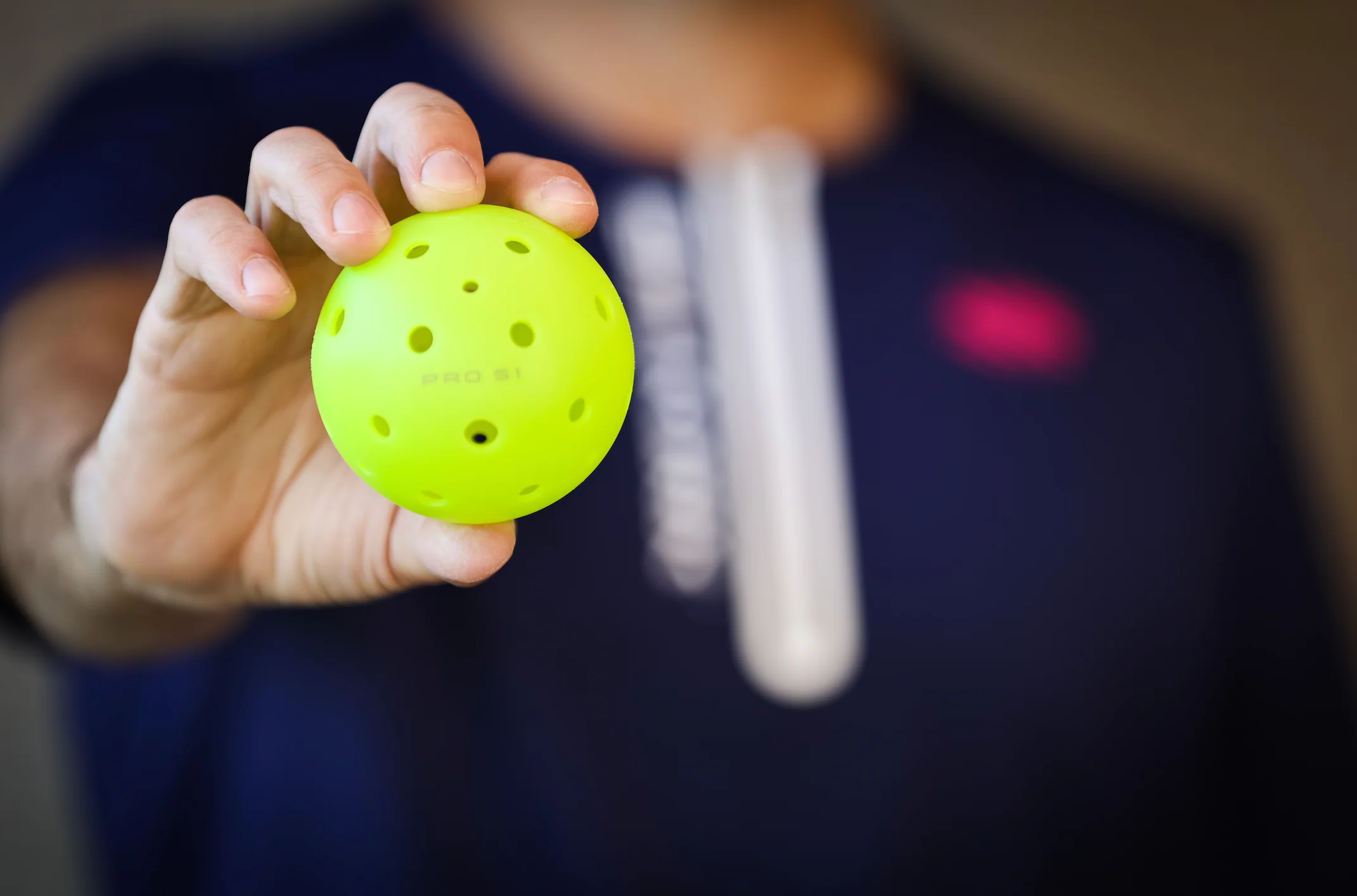 A person holding a bright yellow Selkirk Pro S1 pickleball with 38 holes.