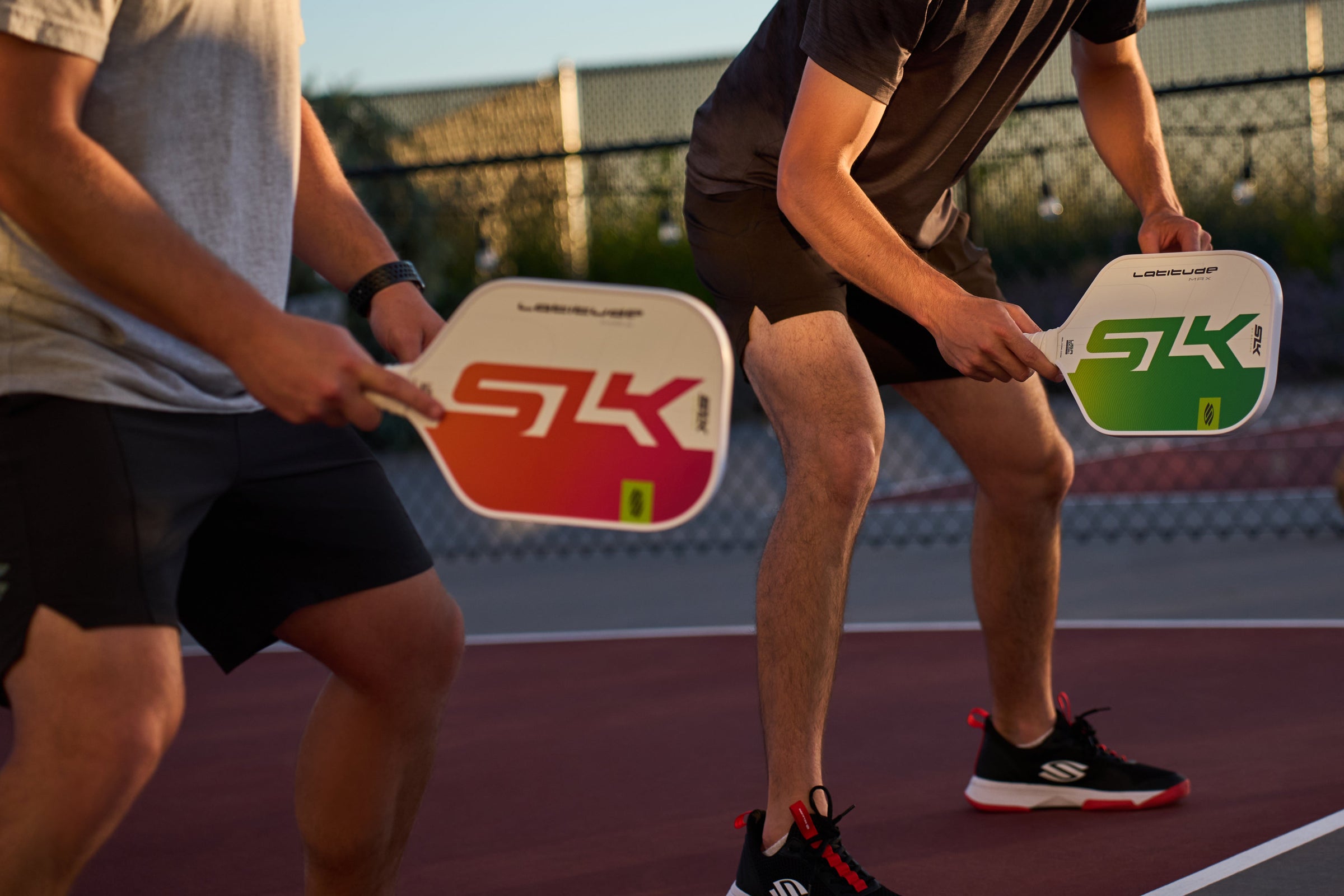 Two men prepare to receive a volley from their opponent as they hold SLK Latitude paddles. 