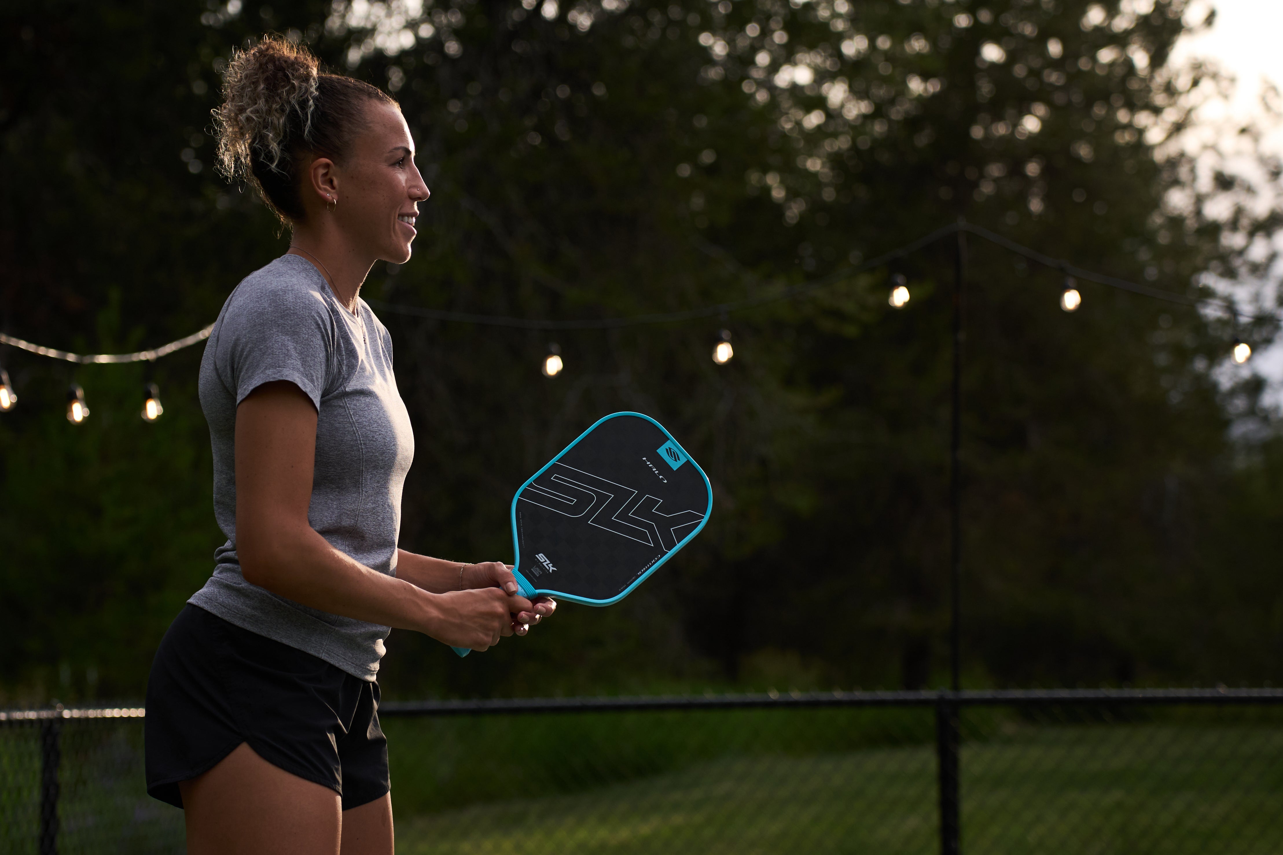 A woman, shown in profile, holds her SLK Halo paddle as she prepares to play pickleball. 