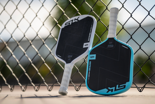 Two ERA Power pickleball paddles rest against a chainlink fence. 