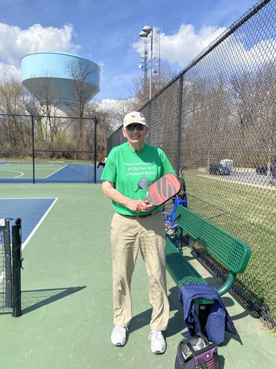 Lowell, a 77-year-old man from Bethesda, MD, holding a pickleball paddle on a court, wearing a green shirt.