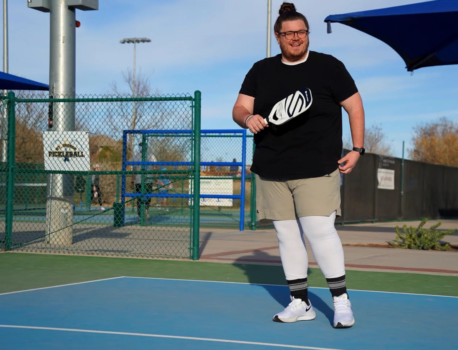 A person standing on a pickleball court, holding a paddle, smiling.