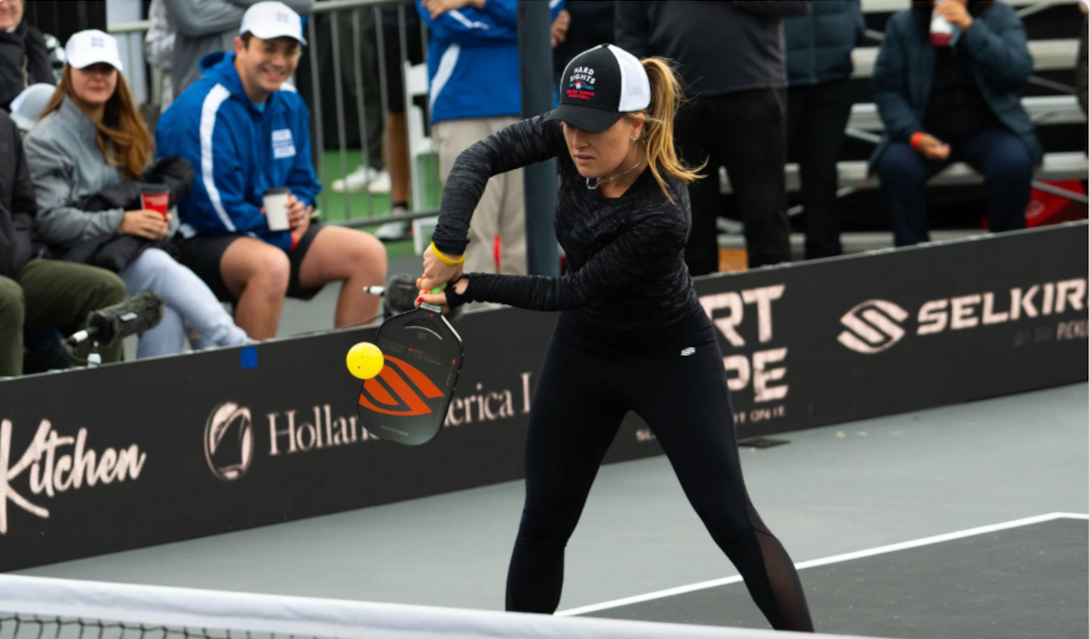 A player preparing to hit a pickleball during a match, with spectators in the background.