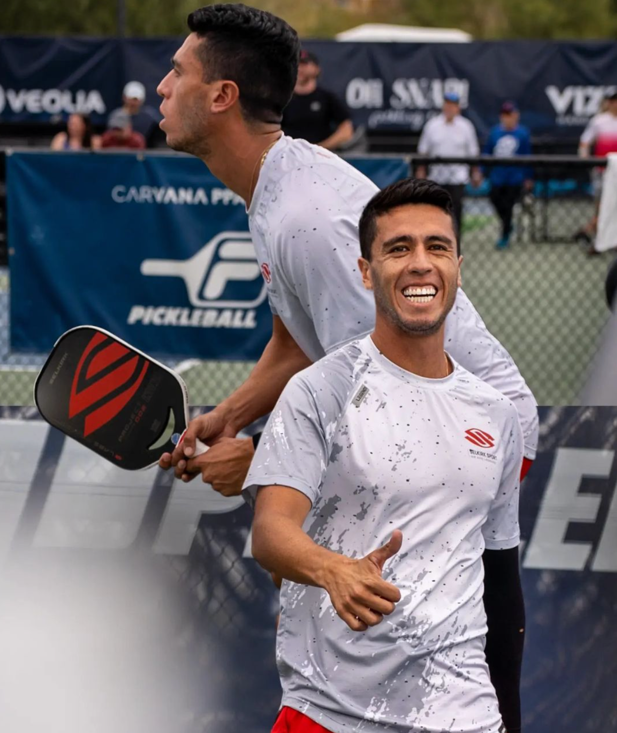 Two pickleball players celebrating during a match, one giving a thumbs up.