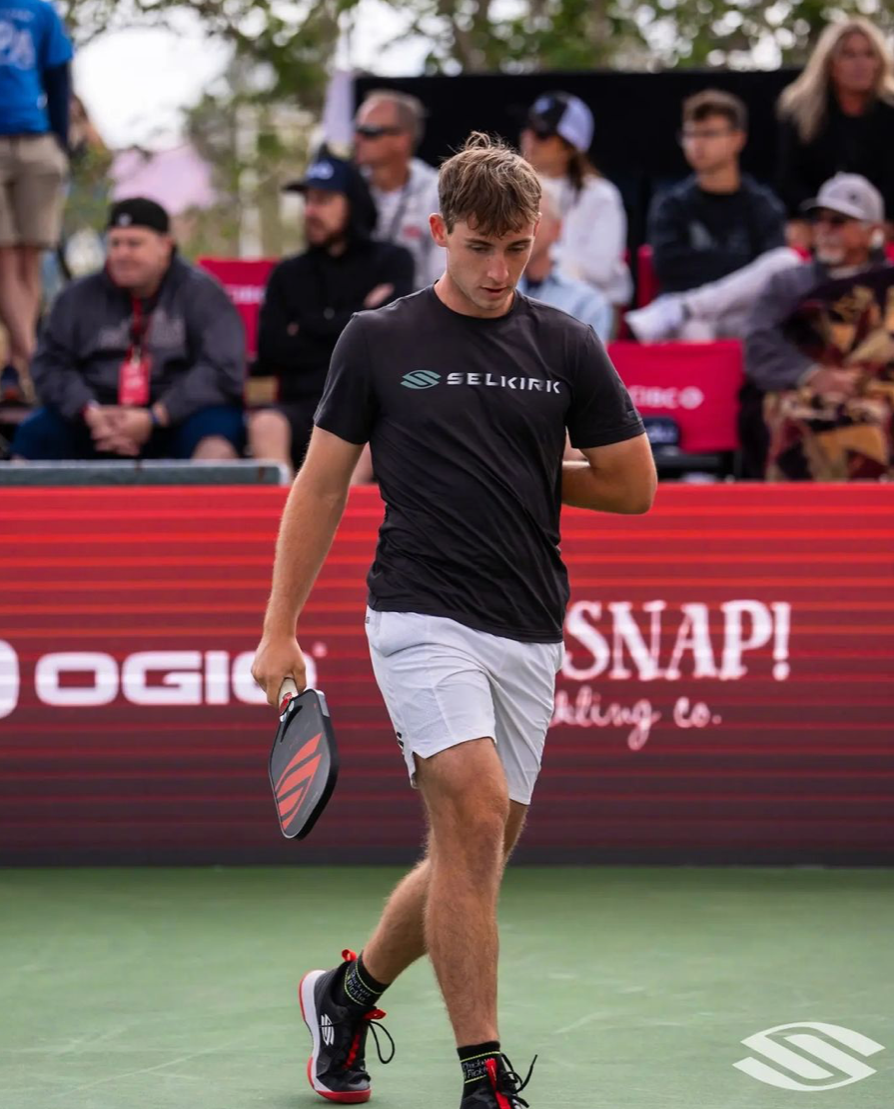 Pickleball pro Dylan Frazier walking on the court with a paddle during a match.