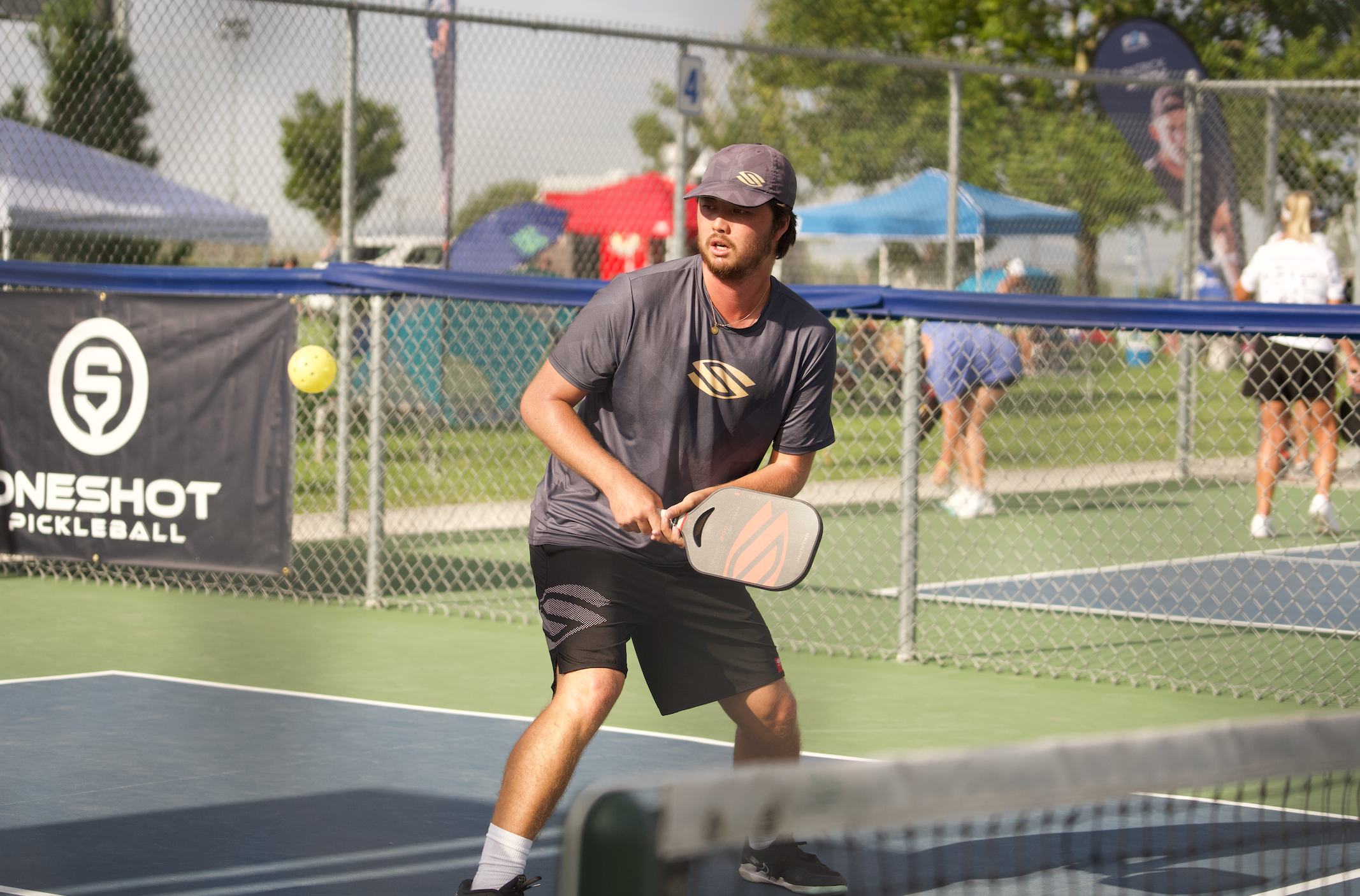 A man prepares for a backhand drive on an outdoor pickleball court. 