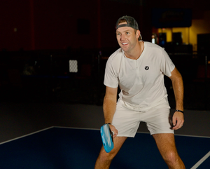 A smiling male pickleball player preparing to serve on a court