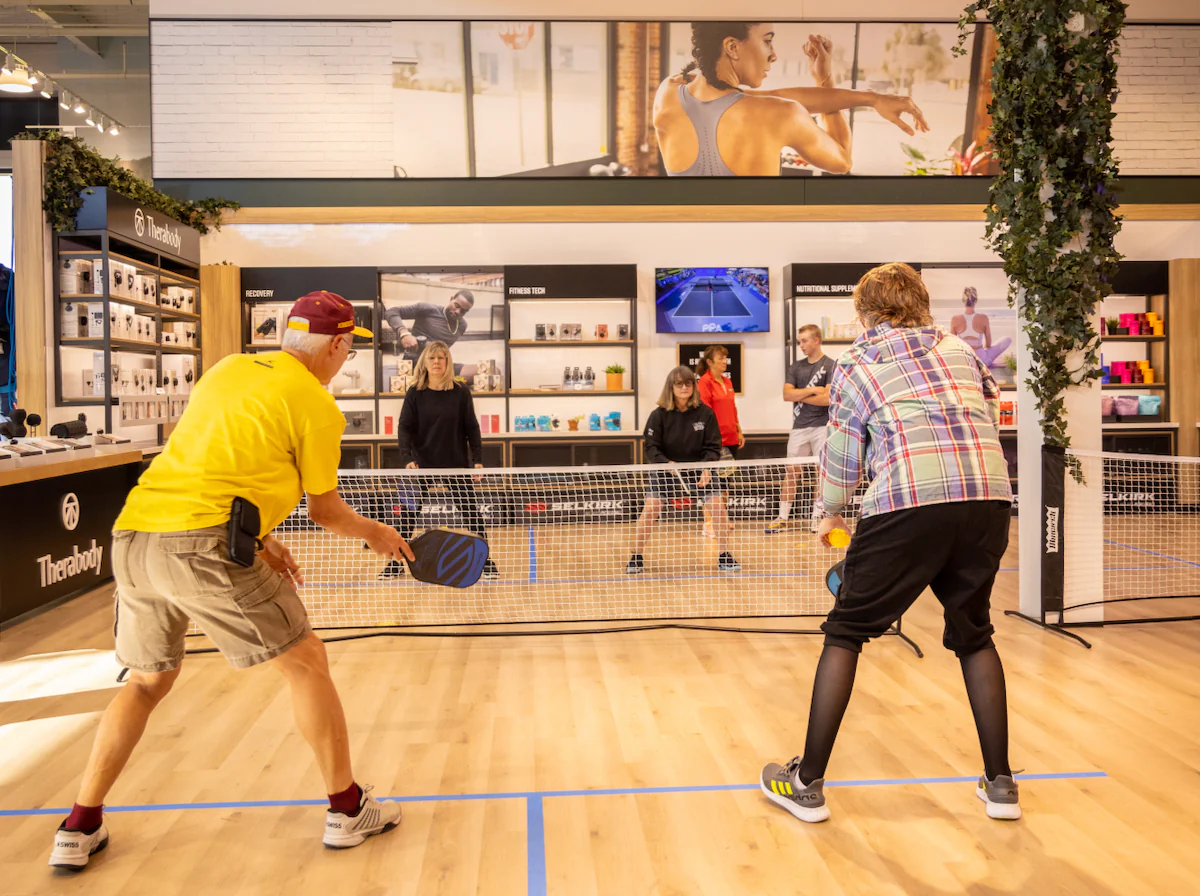 A couple playing pickleball in a store, with others watching.