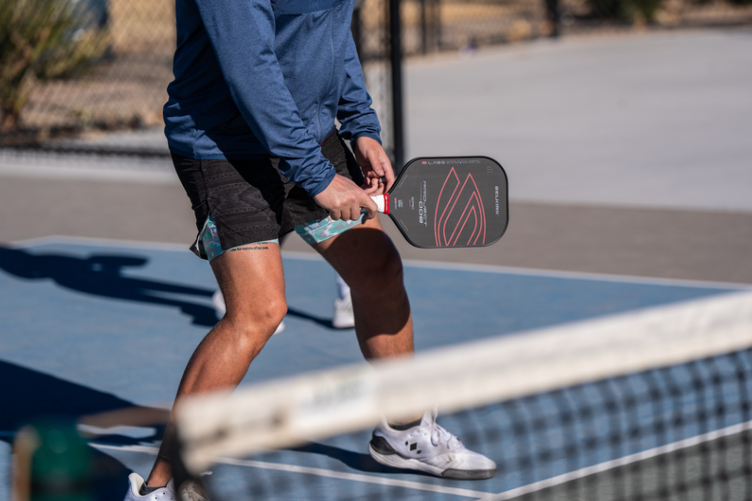 An image shows a mans legs and arms as he prepares to receive a volley with his raw carbon 008 pickleball paddle. 