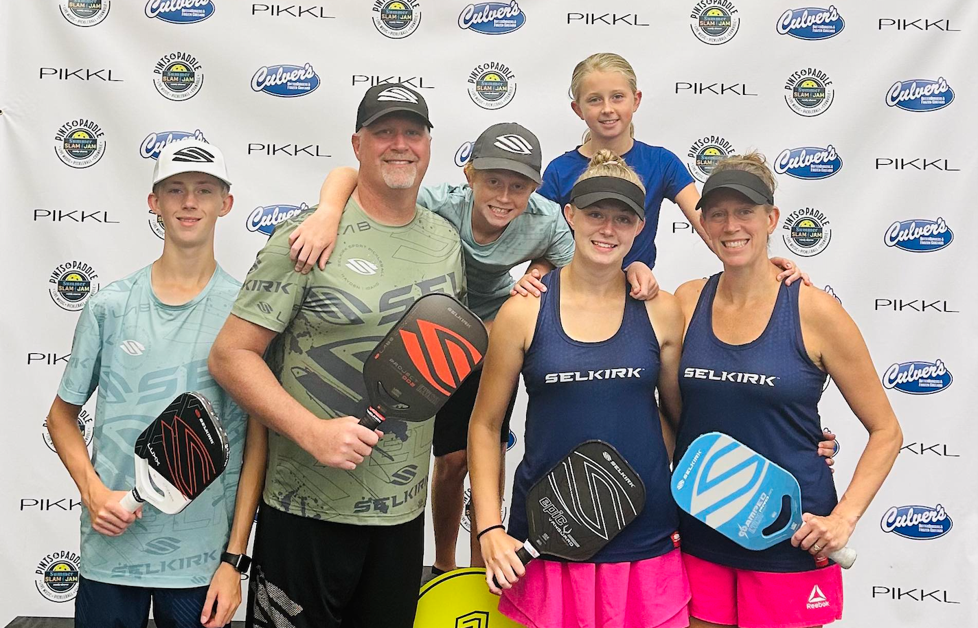The Lund family stands on a podium holding their Selkirk pickleball paddles. 