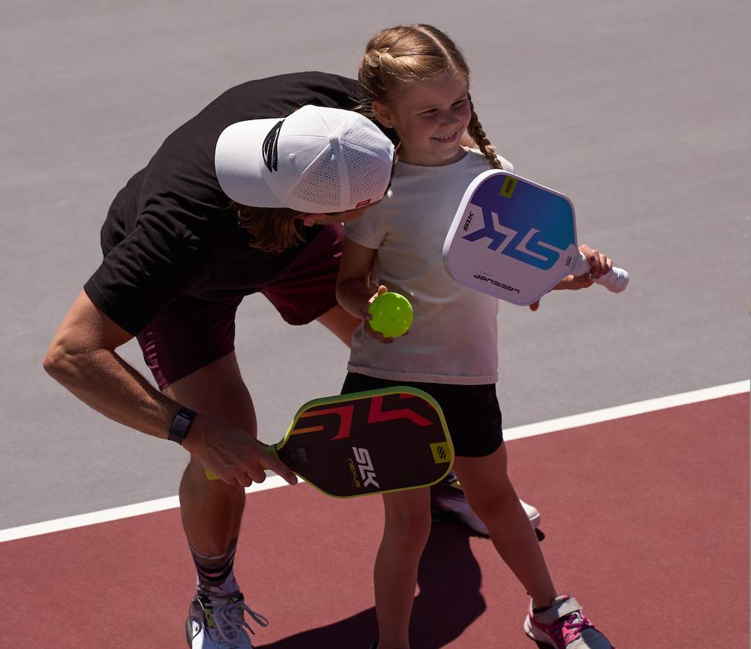 A man hugs his daughter as they hold their pickleball paddles. 