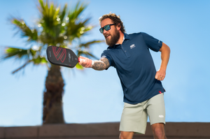 A middle-age man wears sunglasses and Selkirk clothing as he plays pickleball with a LABS Project 008 pickleball paddle. 
