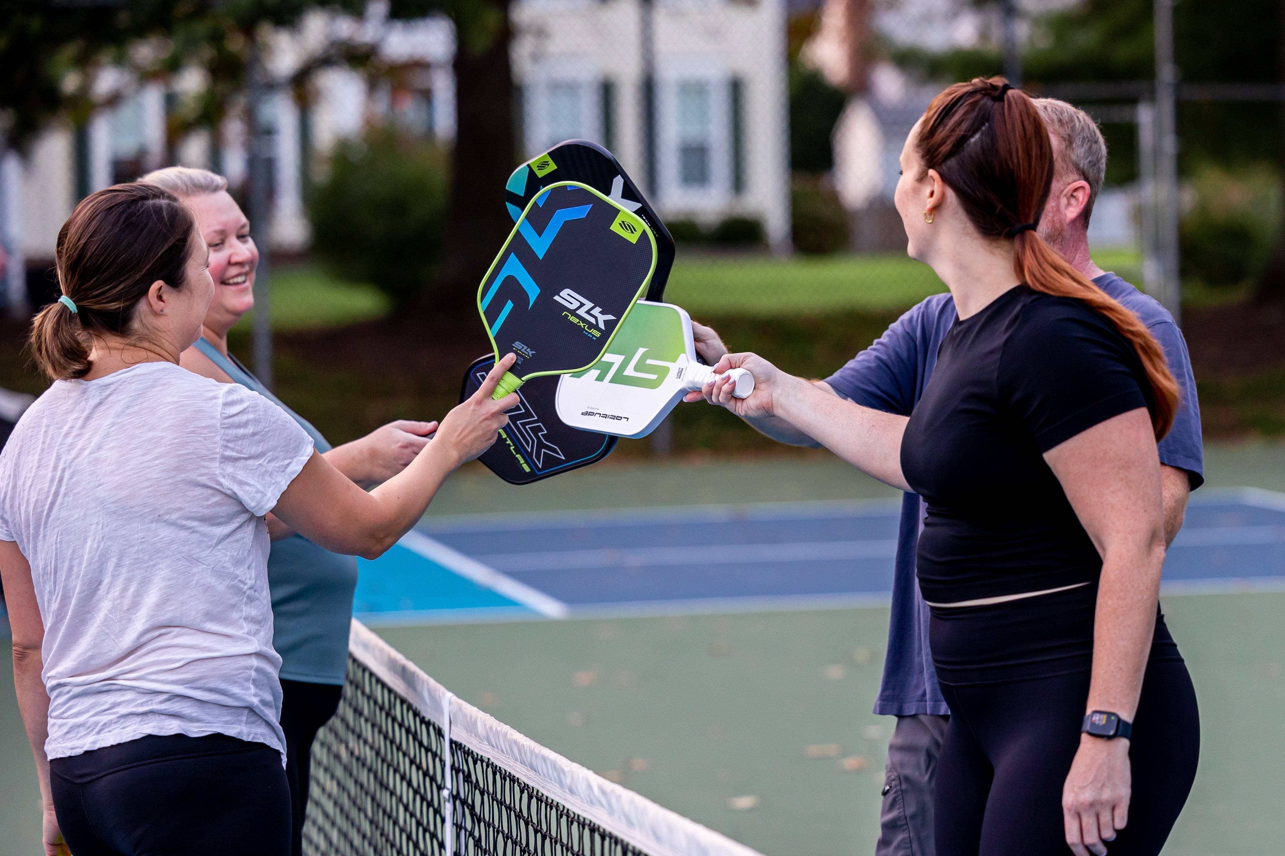 Four people tap Selkirk paddles over a net after a pickleball match on an outdoor court. 
