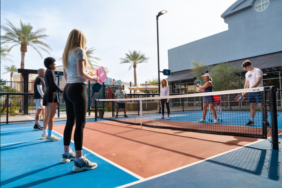 A group of students lines up at the kitchen line on either side of a net to and volleys back and forth. 